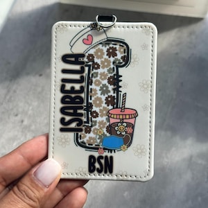 May include: A white badge holder with the name "ISABELLA" in black lettering. The design includes a coffee cup, a nurse's cap with a heart, and a drink with a flower. The letters "BSN" are at the bottom.