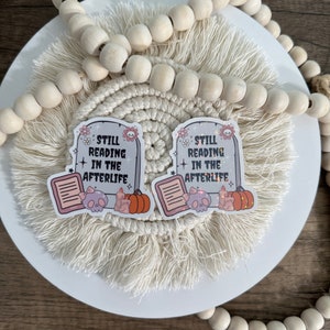 Peut inclure: Deux autocollants blancs avec un design de pierre tombale et le texte "Still Reading in the Afterlife". Chaque autocollant repr&eacute;sente un cr&acirc;ne, un livre et une citrouille.