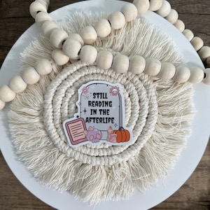 Peut inclure: Un autocollant blanc avec un design de pierre tombale et le texte "Still Reading in the Afterlife". L'autocollant repr&eacute;sente un cr&acirc;ne, un livre, des bougies et une citrouille.