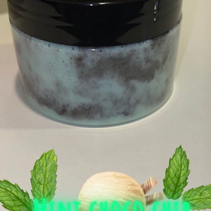 May include: A close-up of a jar of mint chocolate chip body scrub. The jar is black with a white label that says "Mint Choco Chip". The scrub is a light green color with dark brown swirls.