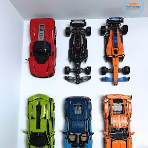 May include: Six different Lego car models displayed on a white wall. The cars are a red Ferrari, a black Mercedes, an orange McLaren, a green Lamborghini, a blue Bugatti, and an orange Lamborghini. The text "CARS NOT INCLUDED" is printed below the cars.