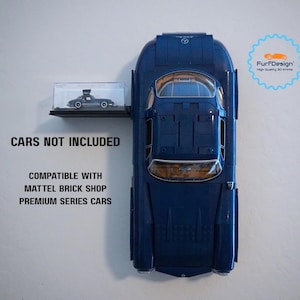 May include: A dark blue toy car with a small display shelf holding a miniature car model. The text "CARS NOT INCLUDED" and "COMPATIBLE WITH MATTEL BRICK SHOP PREMIUM SERIES CARS" are visible. A logo is in the upper right corner.
