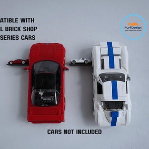 May include: Wall-mounted display shelves holding toy cars. A red car and a white car with blue stripes are displayed. The text "COMPATIBLE WITH MATTEL BRICK SHOP ELITE SERIES CARS" and "CARS NOT INCLUDED" are visible.