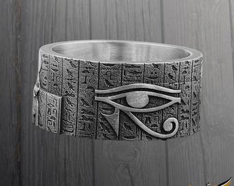 May include: A silver ring featuring an Egyptian Eye of Horus design. The ring is engraved with hieroglyphics.