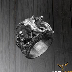 Può includere: Un anello d'argento con un designo dettagliato di un elefante e altri animali. L'anello è in metallo e ha una superficie testurizzata.