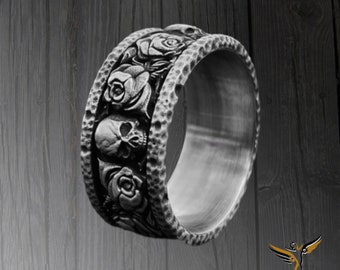 May include: A silver ring with a skull and rose design. The ring is wide and has a textured surface.