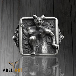 Könnte beinhalten: Ein silberner Ring mit einem detaillierten Design einer gehörnten Dämonenfigur in einem quadratischen Rahmen.