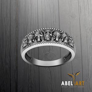 Peut inclure: Une bague en argent avec une rangée de sept têtes de crâne, chacune avec une expression différente. La bague est décorée de petites perles autour des crânes.
