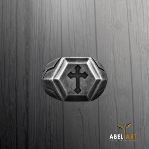 May include: A silver-toned metal ring featuring a central hexagonal face with a recessed cross symbol. The band has a weathered, dark finish with geometric facets surrounding the center, creating a structured and bold appearance for this jewelry piece.