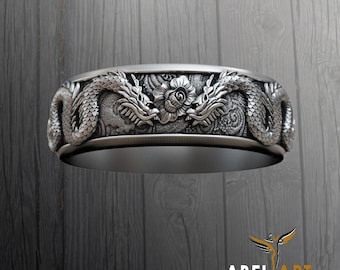 Könnte beinhalten: Ein silberner Ring mit einem detaillierten Design aus zwei sich gegenüberstehenden Drachen mit einer Rose in der Mitte. Der Ring liegt auf einem hölzernen Untergrund.