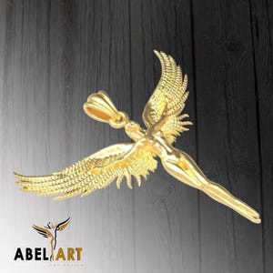 May include: A gold-colored pendant featuring a detailed angel figure with outstretched wings. The angel is depicted in a flying pose with its arms raised.