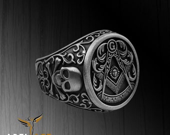 May include: A silver ring featuring a skull and crossbones design on one side and a Masonic symbol with a compass and square on the other.