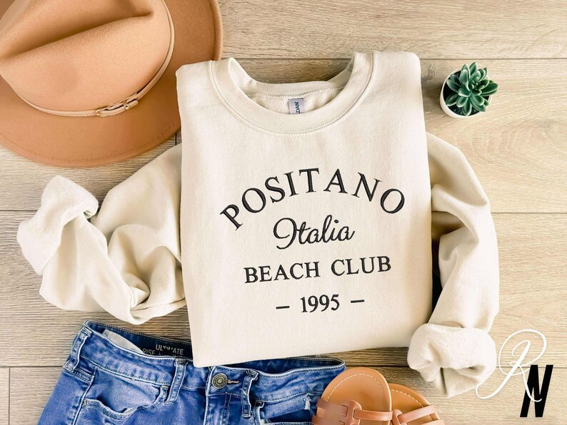 May include: A cream-colored sweatshirt with black text that reads "Positano Italia Beach Club - 1995 -"