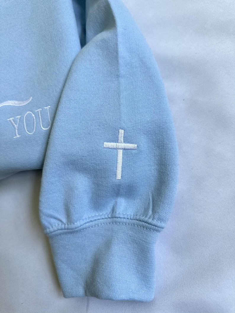 May include: A light blue sweatshirt with a white embroidered cross on the sleeve and the word "YOU" on the front.