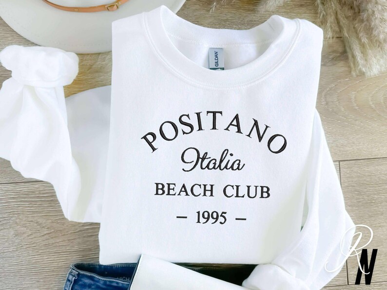May include: White sweatshirt with black text that reads "Positano Italia Beach Club - 1995 -"