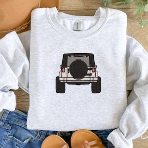 May include: A gray sweatshirt with a black and white illustration of a Jeep on the front. The Jeep is facing away from the viewer and has a spare tire on the back.