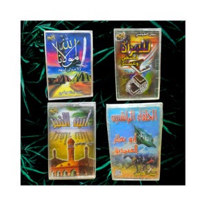 May include: Four rectangular books with Arabic text and colourful illustrations. The books feature titles in Arabic script, with images of a mosque, a ship, and other religious symbols. The books are displayed against a dark green background.