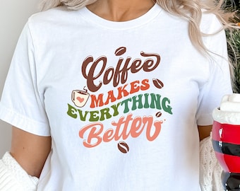 Puede incluir: Camiseta blanca con el texto "Coffee makes everything better" en letras estilizadas de colores. Se incluye una taza de café con un corazón en el diseño.