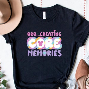 May include: Black t-shirt with a colourful graphic that says "BRB... CREATING CORE MEMORIES" with a pink Mickey Mouse head in the middle of the word "CORE".