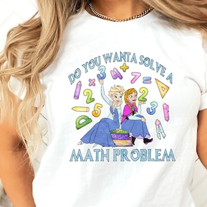 May include: White t-shirt featuring a graphic of two cartoon girls, one with blonde hair and one with red hair, holding up numbers and mathematical symbols. The text "Do you want to solve a math problem?" is printed below the graphic.
