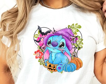 Pode incluir: Uma camiseta branca com um design de Halloween azul, roxo e verde com um personagem de desenho animado Stitch usando um chapéu de bruxa e segurando uma abóbora.