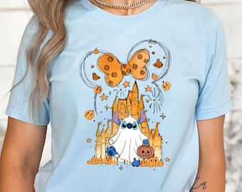 Pode incluir: Camiseta azul claro com uma ilustração de desenho animado do Stitch vestido de fantasma segurando uma abóbora talhada na frente de um castelo com um grande laço laranja.
