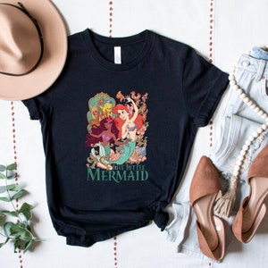 Może przedstawiać: Czarny T-shirt z nadrukiem graficznym przedstawiającym Ariel, Floundera i Urszulę z bajki Mała Syrenka. Pod nadrukiem znajduje się napis "The Little Mermaid".