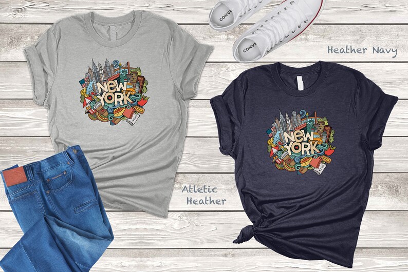 May include: Two t-shirts with a graphic design of New York City landmarks and icons. The shirt on the left is athletic heather and the shirt on the right is heather navy.