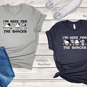 May include: Two t-shirts with the text "I'm here for the snacks" and a cartoon image of Mickey Mouse, a Dalmatian, a cupcake, and a milkshake. The t-shirts are in athletic heather and heather navy.