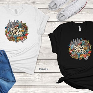 May include: Two t-shirts with a doodle design of New York City landmarks and the text "New York". The t-shirt on the left is white and the t-shirt on the right is black.