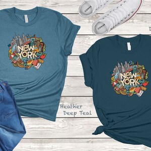 May include: Two t-shirts with a doodle design of New York City landmarks and the text "New York" in a circle. The t-shirt on the left is heather deep teal and the t-shirt on the right is deep teal.