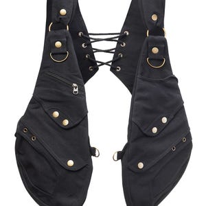 Könnte beinhalten: Eine schwarze Canvas-Weste mit mehreren Taschen und goldfarbenen Beschlägen. Die Weste hat einen Schnürrücken und verstellbare Träger.