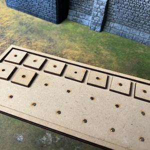 May include: A wooden board with nine square cutouts and multiple small holes. The board is designed to hold miniature figures or other small objects.