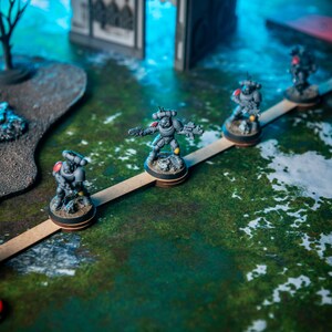 Puede incluir: Un grupo de figuras en miniatura grises y negras de pie en un puente de madera. Las figuras sostienen armas y est&aacute;n posicionadas en l&iacute;nea. El puente est&aacute; sobre una superficie verde y blanca.
