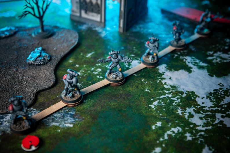 Puede incluir: Un grupo de figuras en miniatura grises y negras de pie en un puente de madera. Las figuras sostienen armas y est&aacute;n posicionadas en l&iacute;nea. El puente est&aacute; sobre una superficie verde y blanca.