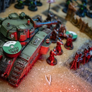 Peut inclure: Un char vert et rouge avec un jeton circulaire vert et blanc qui dit "Take Aim Orders". Le char a le numéro "06" sur le côté. Le char est sur une table avec d'autres figurines miniatures.