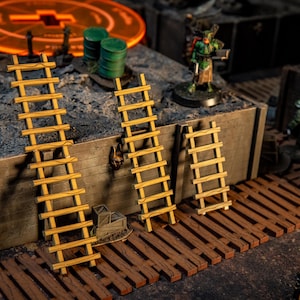 Peut inclure: Trois échelles miniatures en bois de différentes tailles, appuyées contre une surface texturée. Les échelles sont brun clair avec des barreaux visibles. La scène comprend des figurines miniatures et d'autres accessoires de jeu, suggérant un thème de jeu de table.