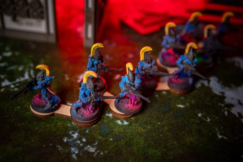 Puede incluir: Una fila de figuras en miniatura azules y amarillas con pistolas, de pie sobre bases circulares. Las figuras est&aacute;n dispuestas en l&iacute;nea sobre una superficie verde.