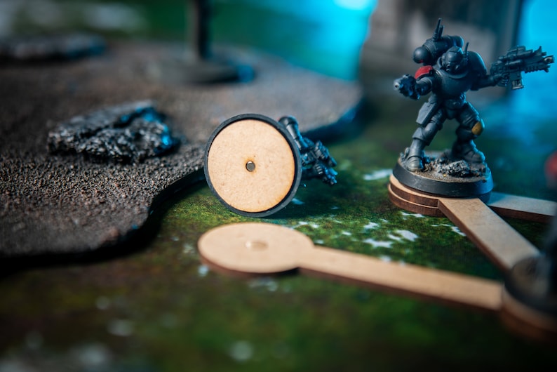 Puede incluir: Una figura de Space Marine en miniatura pintada en negro y amarillo con una hombrera roja, de pie sobre una base redonda de madera. La figura sostiene un arma y est&aacute; en una postura de combate. La figura est&aacute; sobre una superficie texturizada verde y marr&oacute;n.