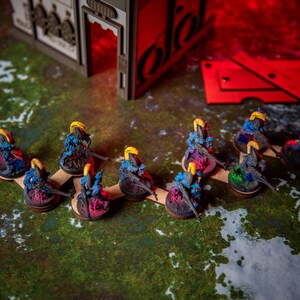 Puede incluir: Una l&iacute;nea de figuras en miniatura pintadas de azul y amarillo de pie sobre bases de madera. Las figuras sostienen armas y est&aacute;n dispuestas en formaci&oacute;n de l&iacute;nea.