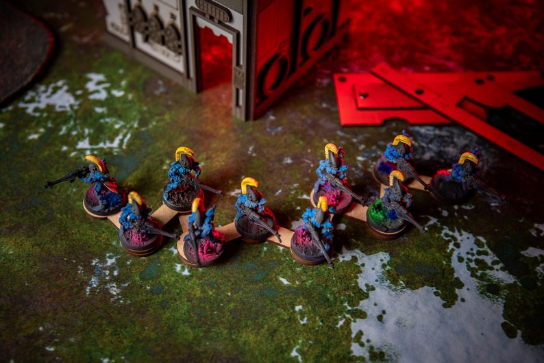 Puede incluir: Una l&iacute;nea de figuras en miniatura pintadas de azul y amarillo de pie sobre bases de madera. Las figuras sostienen armas y est&aacute;n dispuestas en formaci&oacute;n de l&iacute;nea.