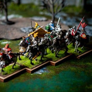 May include: A group of miniature knights on horseback, painted in silver, gold, and red, with colorful flags and shields. The knights are arranged in a line on a wooden base, with green grass and a stream in the background.