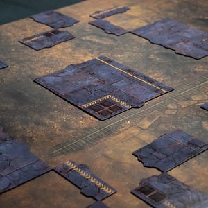May include: A tabletop gaming mat with modular terrain pieces. The mat has a brown and green background with a grid pattern. The terrain pieces are dark blue with a cracked texture and yellow accents, resembling a futuristic cityscape.