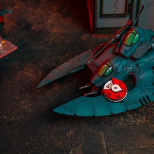 May include: A teal blue spaceship model with a red and white dial labelled "Wind" with numbers 1-6 and 788. The spaceship has a green cockpit and a long, thin gun.