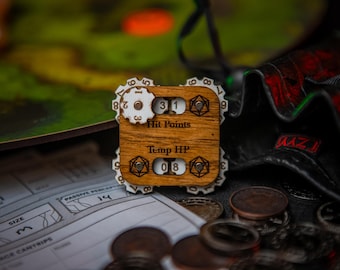 May include: A wooden character sheet tracker for tabletop role-playing games. The tracker has dials for hit points, temporary hit points, and other stats. The tracker is made of wood and has a natural finish. The tracker is sitting on a table with other game pieces.