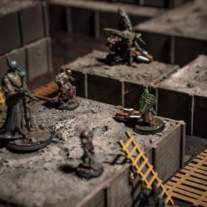 K&ouml;nnte beinhalten: Eine Tabletop-Gaming-Szene mit Miniaturfiguren auf einem modularen Gel&auml;nde. Die Figuren umfassen Fantasy-Charaktere und -Kreaturen, mit einer gelben Leiter und grauen, strukturierten Bl&ouml;cken. Die Szene ist mit weichem, diffusem Licht beleuchtet.