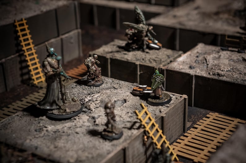 K&ouml;nnte beinhalten: Eine Tabletop-Gaming-Szene mit Miniaturfiguren auf einem modularen Gel&auml;nde. Die Figuren umfassen Fantasy-Charaktere und -Kreaturen, mit einer gelben Leiter und grauen, strukturierten Bl&ouml;cken. Die Szene ist mit weichem, diffusem Licht beleuchtet.