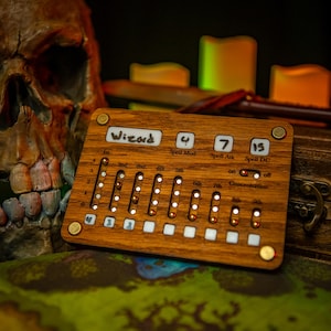 May include: A wooden tabletop game tracker with the word "Wizard" printed on it. The tracker has a series of sliders and dials with numbers and labels like "Spell Mod", "Spell Atk", and "Spell DC".