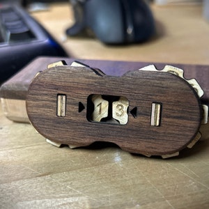 Puede incluir: Un contador de madera con dos engranajes que muestran los números "1" y "3". El contador está hecho de madera oscura y tiene un borde de madera clara.