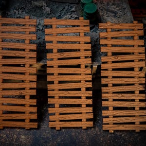 Puede incluir: Tres mini-palés de madera con un acabado detallado de vetas. Los palés son de color marrón cálido y están dispuestos en fila. Probablemente para juegos de mesa o construcción de modelos.